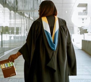Image of woman with graduation gown on holding a MLIS book